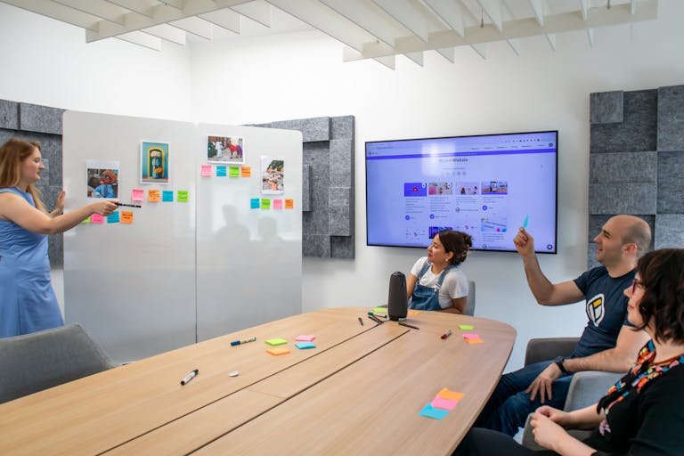 A group of coworkers engaged in a creative brainstorming session with colorful Post-it notes and a digital display.